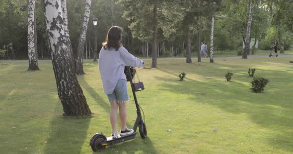 Friends ride electric scooter or in the park at sunset. Ecological transportation.