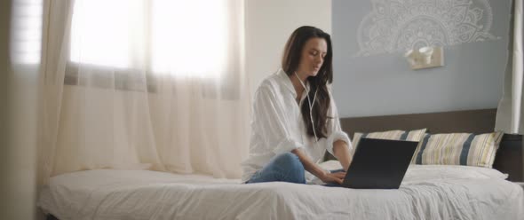 A young woman speaking to someone through earphones while working on her laptop