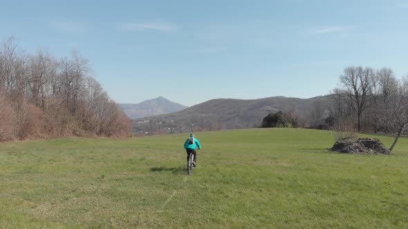 Aerial: man having fun by riding mountain bike in the grass on sunny day, scenic alpine landscape