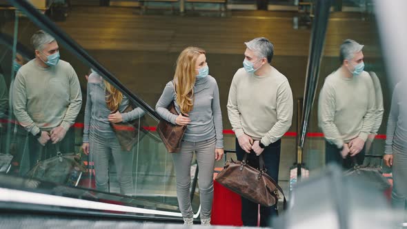 Happy Man and Woman Wearing Protective Medical Masks Riding Up on Escalator at Airport Building with