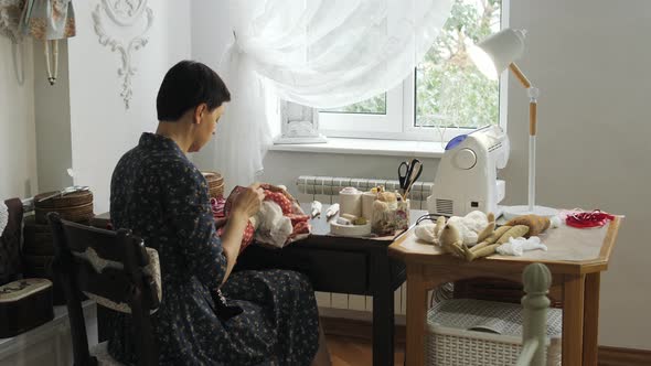 Woman sitting and sewing a doll alt