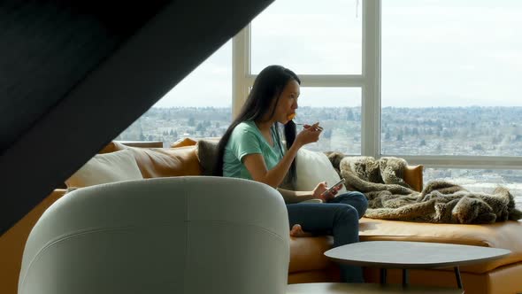 Woman using mobile phone while having breakfast in living room