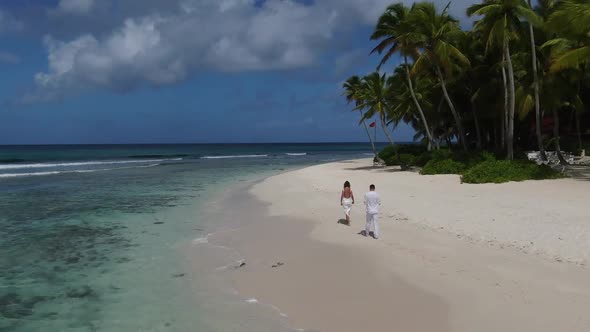 Aerial View of Two People Wearing White Clothes Walking on a Tropical Beach