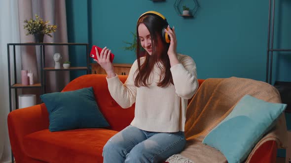 Overjoyed Young Woman in Wireless Headphones Dancing Singing on Cozy Couch in Living Room at Home