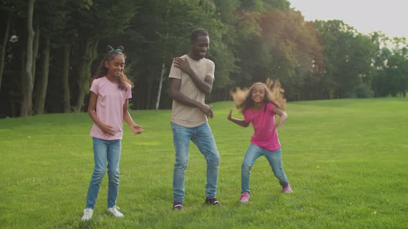 Joyful Father and Daughters Dancing on Park Lawn