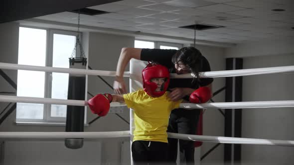 A Guy Coach Talking with a Little Boy Boxer and Massages His Shoulders on the Ring