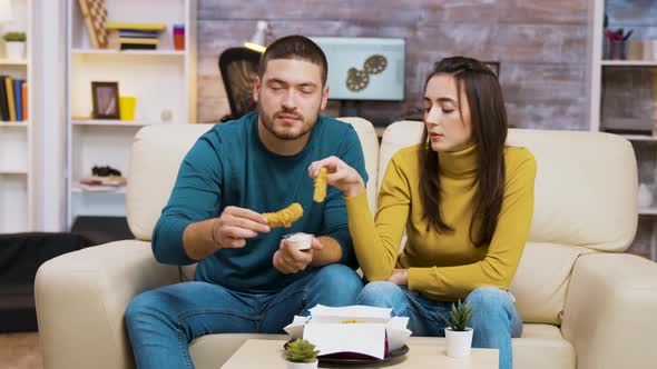 Young Couple Sitting on Couch Eating Fried Chicken