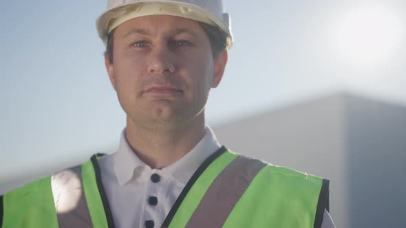 Closeup Portrait of Proud Confident Caucasian Man in Hard Hat Posing in Sunrays Outdoors