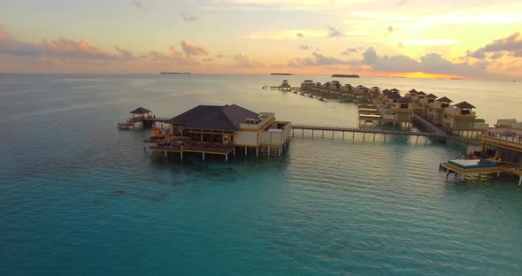 Aerial drone view sunset scenic tropical island, resort hotel with overwater bungalows, Maldives.