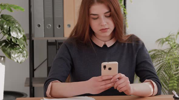 Beautiful caucasian red hair female student using smartphone or cell phone.