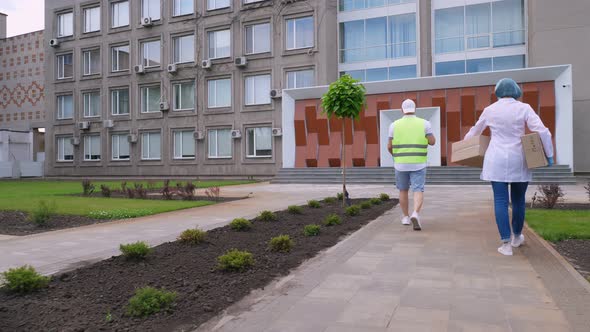 Courier and Doctor, in Protective Masks, Gloves, Going Through Courtyard of Hospital or Medical