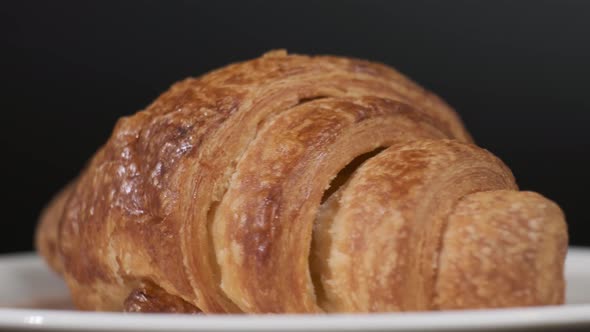 Croissant on white plate rotating in front of camera on black background