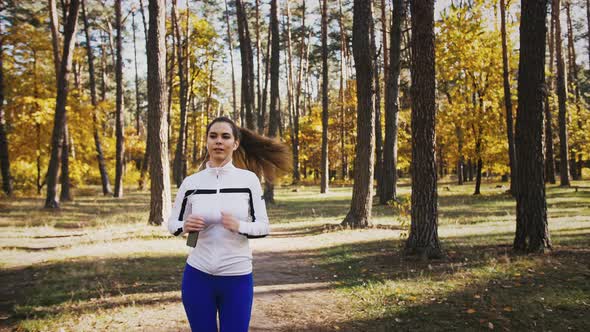 Woman in Sportswear Listening to Music Through Earphones Connected to Cellphone While Jogging in