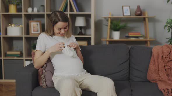 Young Woman Holding Baby Boots on Pregnant Tummy at Home