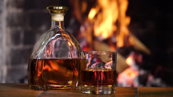 Bottle and Glass with Whiskey or Cognac on the Background of Fire in the Fireplace