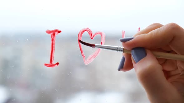 Female Hand Draws Text I LOVE you on the Window with Paint