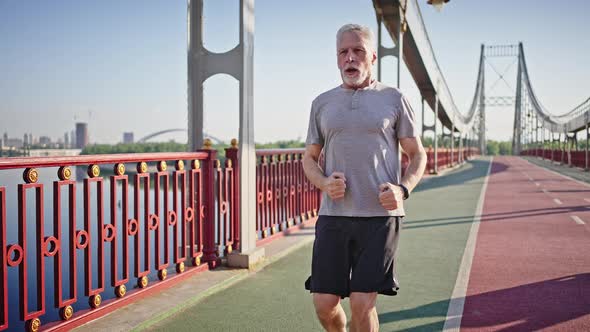 Elderly Man Jogs on Pedestrian Bridge Stopping to Rest