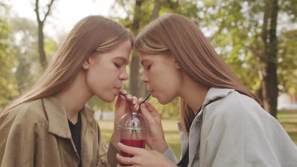 Identical Twin Sisters Enjoying Drink in Park