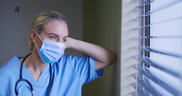 Portrait of caucasian female doctor wearing face mask looking through the window in hospital room