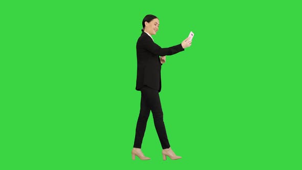 Young Female in a Suit Having Business Video Call on Her Phone on a Green Screen, Chroma Key.