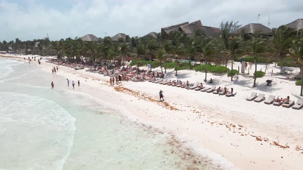 Aerial drone shot over beach in Tulum, Mexico. People chilling, laying around, swimming. Resorts and