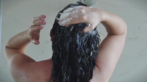 Pretty Young Woman Washes Away the Shampoo From Her Hair While Standing Under a Warm Shower Stream