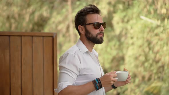 Attractive Handsome Man In Sunglasses Relaxing In Resort And Having Breakfast. Man Drinking Coffee.