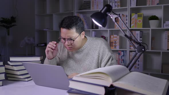 Serious man working on laptop at night, determining information with stressed face on working table