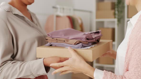 Woman Handing Package and Clothes to Female Customer