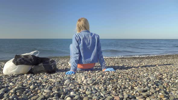 a woman in a denim suit is sitting on the seashore after garbage collection,