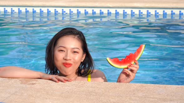 Happy Asian woman eating watermelon at poolside
