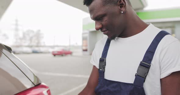 Black African Gas Station Worker Holding a Pistol to Refuel a Car