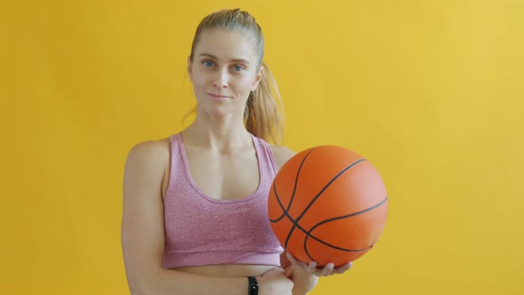 Slow Motion Portrait of Beautiful Girl Throwing Basketball and Smiling on Yellow Background