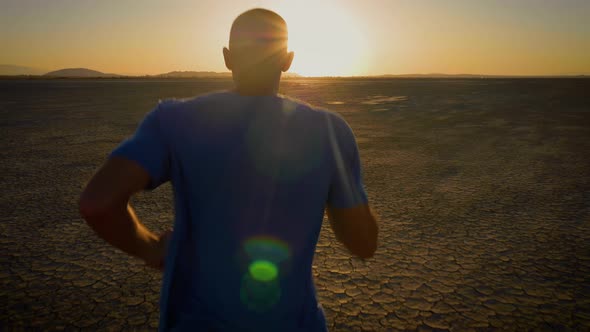 Athletic man working out with battle ropes on a dry lake at sunset