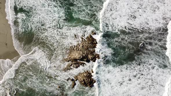 waves break around a small rock in front of the beach of rena majore on sardinia's north-west coast,