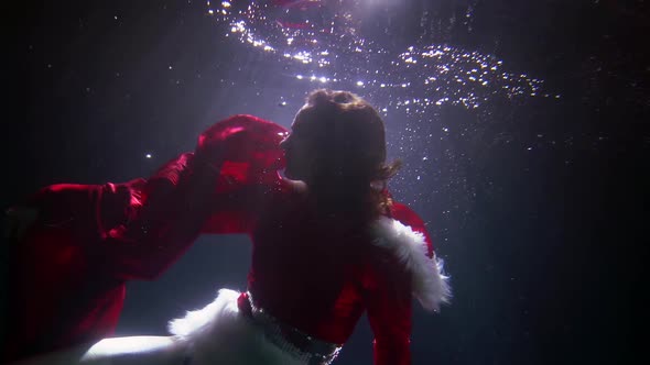 An Attractive Woman in a Red Christmas Dress with White Fur Is Under the Water Spinning