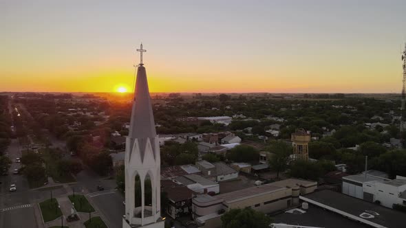 Aerial parallax shot of a church bell tower on a small town at sunset