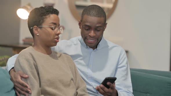 Portrait of Couple Reacting to Loss on Smartphone Sitting on Sofa