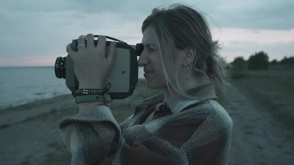 Woman Using Retro Film Camera on Lakeshore in Evening