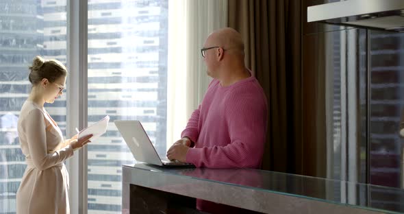 A Man in Glasses and a Pink Sweater Is Typing on a Laptop at the Dictation of His Business Partner