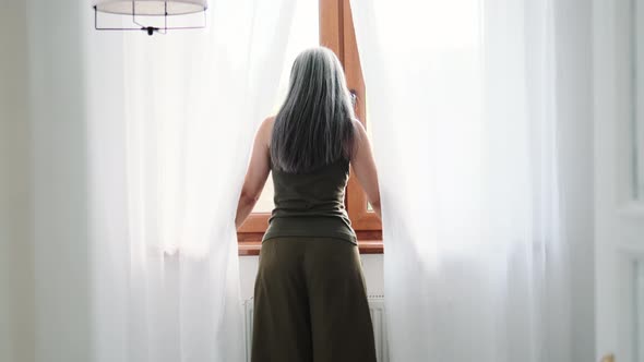 Back view of grey-haired woman looking at window