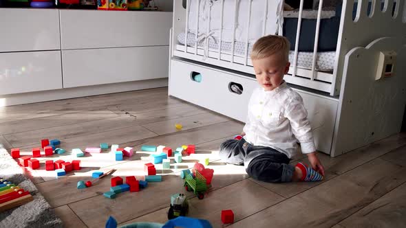 Little Cute Boy Plays with Toy Car and Blocks at Home