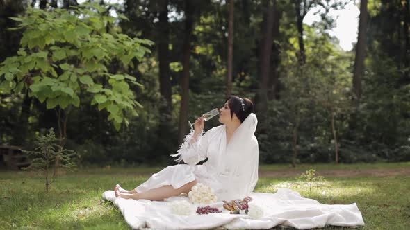 Wedding Bride in Boudoir Dress Sitting in Morning Garden Drinking Champagne Woman in Night Gown Veil