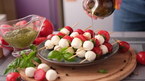 Pouring Olive Oil on Caprese Canapes with Cherry Tomatoes and Mozzarella Cheese Balls
