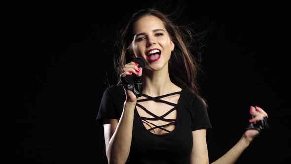 Girl in a Microphone Sings Driving Songs and Smiles. Black Background. Slow Motion