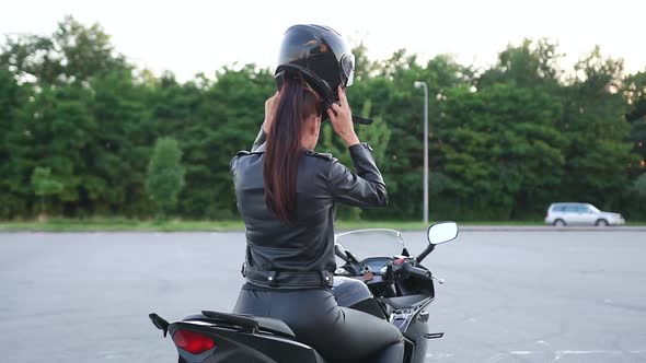 Woman in Biker's Leather Clothes Sitting on Luxurious Motorbike and Putting on Protective Helmet