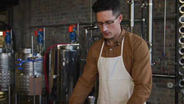 Portrait of serious caucasian man working at gin distillery, using equipment and looking to camera