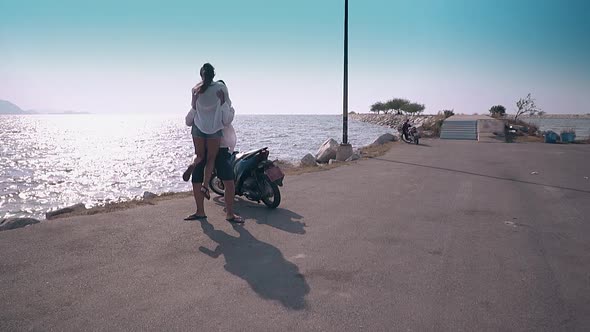 Guy in Cap Lifts and Twists Lady on Embankment Against Ocean