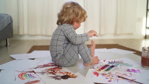 little boy of two years old draws with paints sitting on the floor