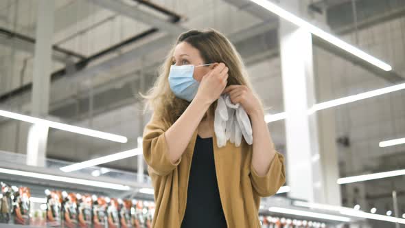 A Young Girl in a Supermarket Puts on a Protective Medical Mask and Rubber Gloves To Protect Against
